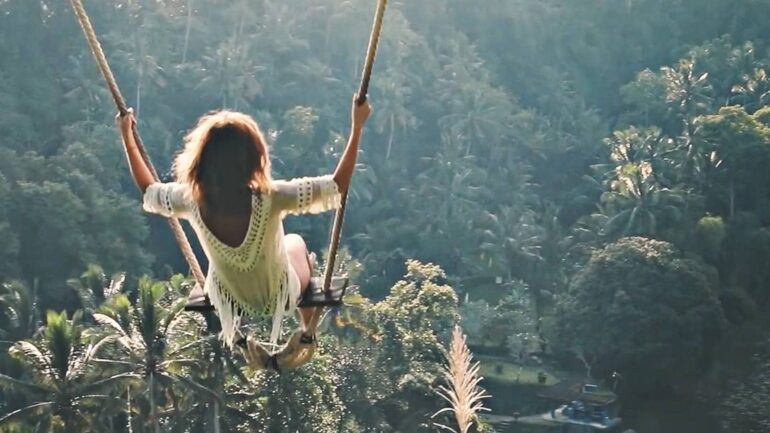 Woman on swing over lush forest, enjoying nature.