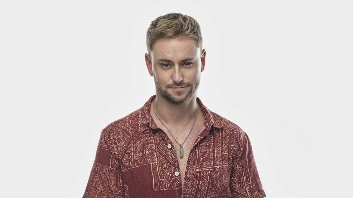 Kenn Colt in a red patterned shirt, hands folded, with a reflective smile, expressing the emotion behind his music.